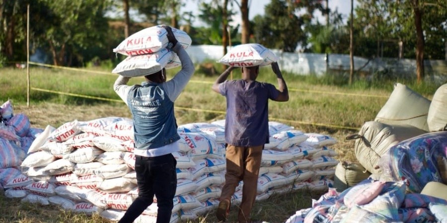 Two men with their backs to camera, carrying sacks of food