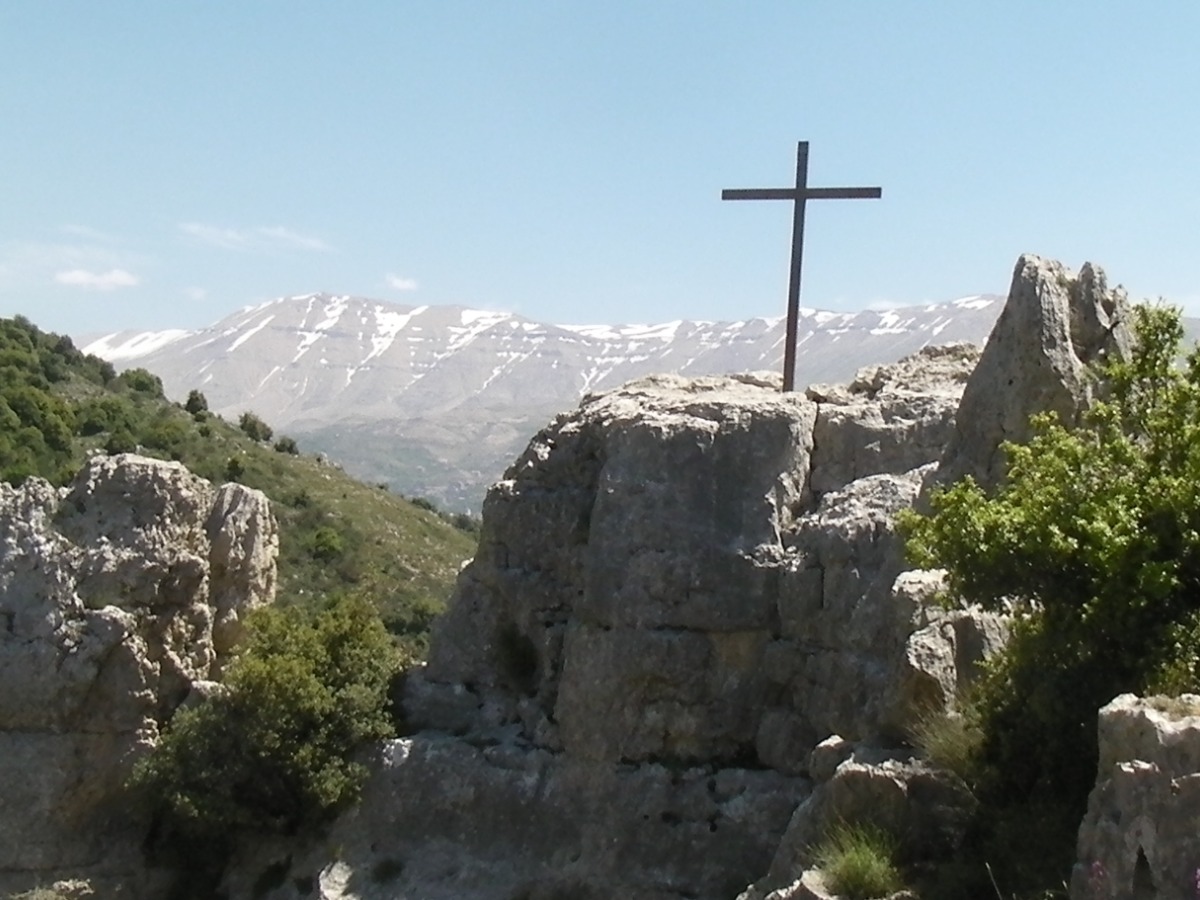 A cross on top of a rocky outcrop with mountains in the background