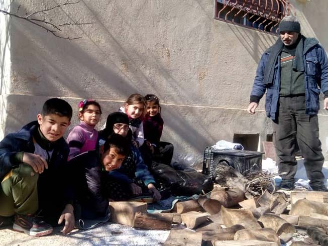 A man stands, and a woman sits with a group of children, all dressed in winter clothes