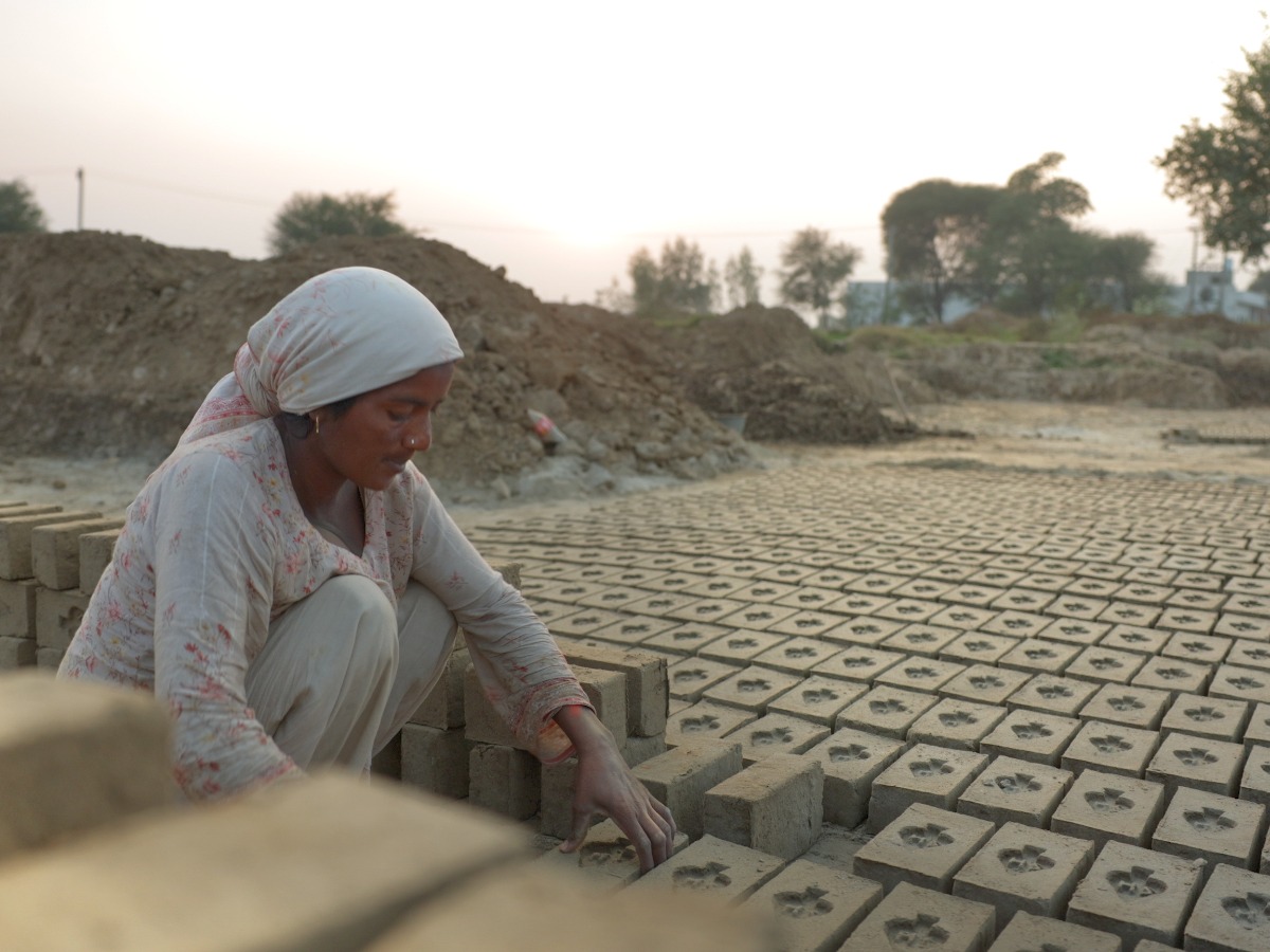 A woman squatting down to make bricks