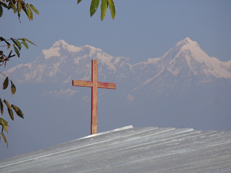 A metal cross on a tin roof with snow-covered mountains in the background