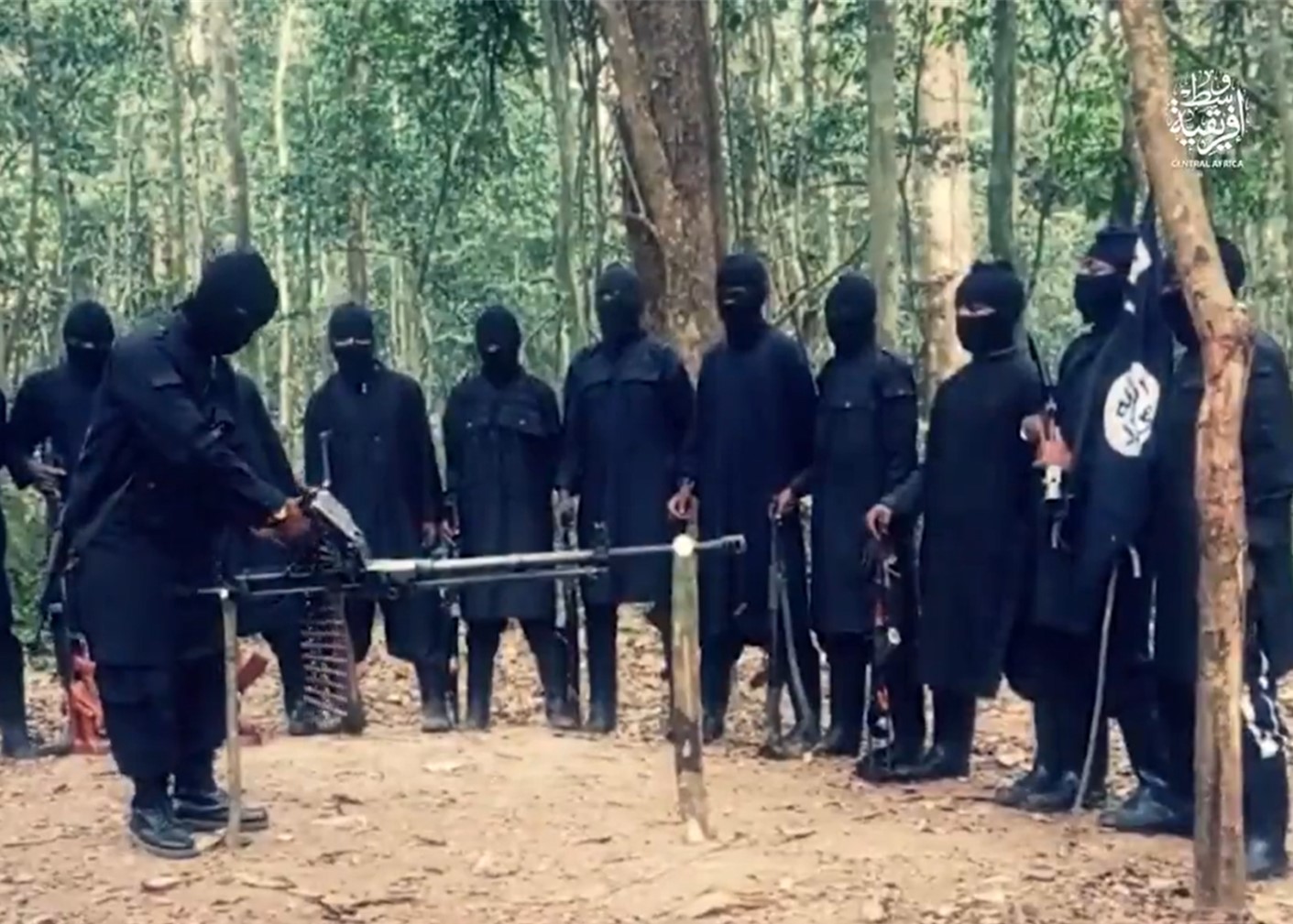 Men dressed in black in woodland. One is demonstrating a machine gun