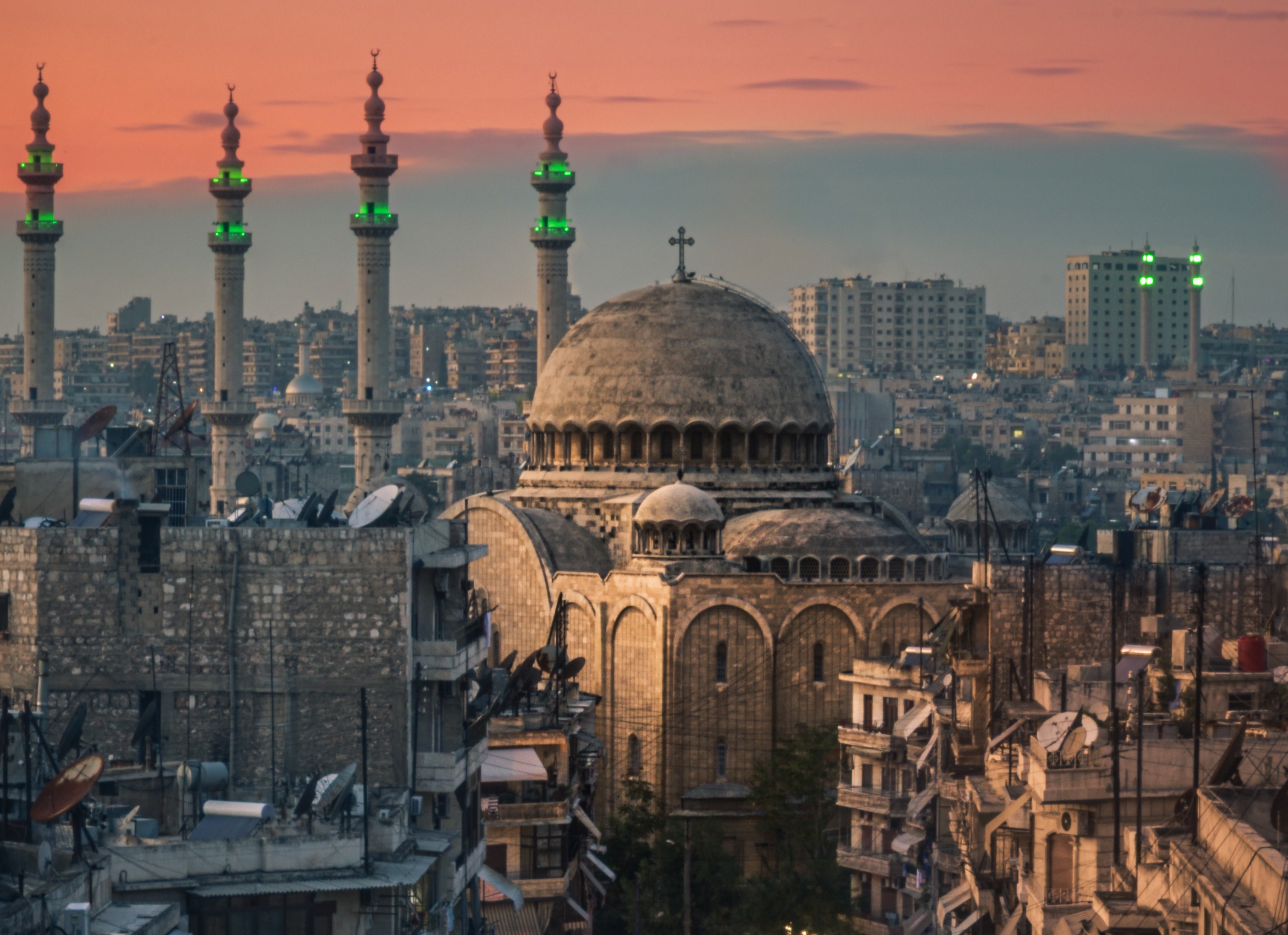 A city at dusk, with a domed church building in the foreground and four minarets in the background