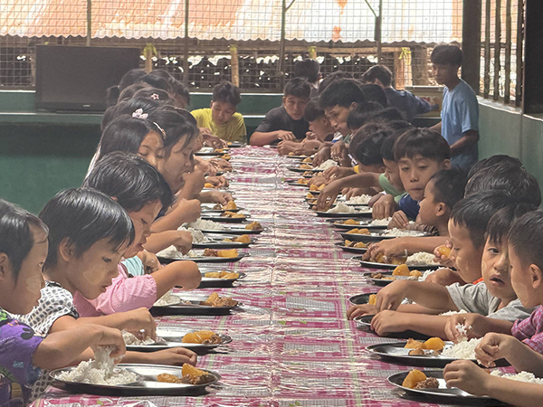 Children sat along a long table, eating rice
