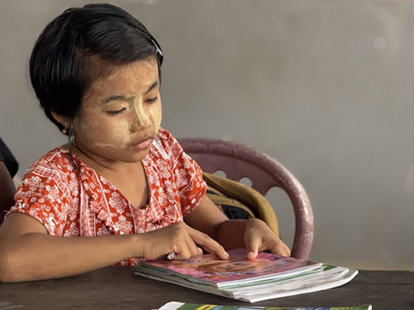 A young girl wearing sun cream sat at a table looking at her school books