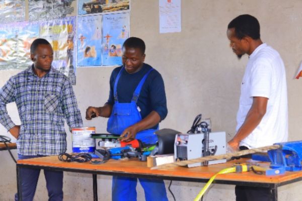 Three men collaborate at a table, using tools while engaging in practical skills and faith-based training.