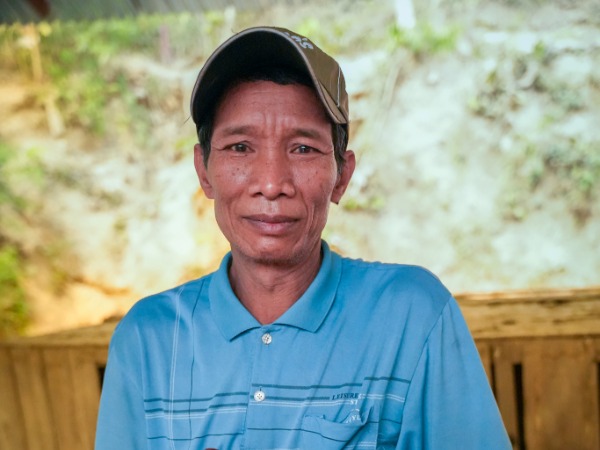 A man in a rural setting, wearing a cap and a blue polo shirt