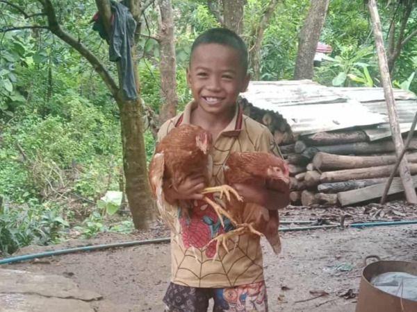 A boy in a rural setting holding two chickens