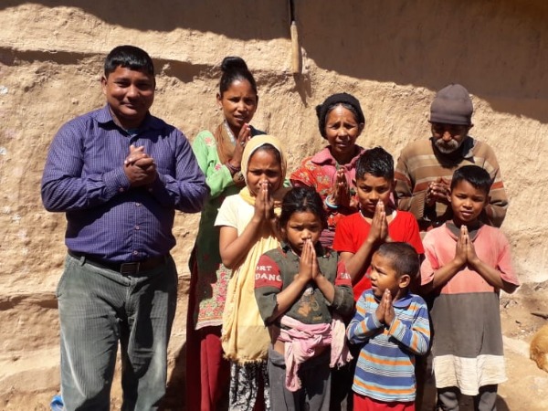 A group of men, women and children, hands clasped together, in a rural setting