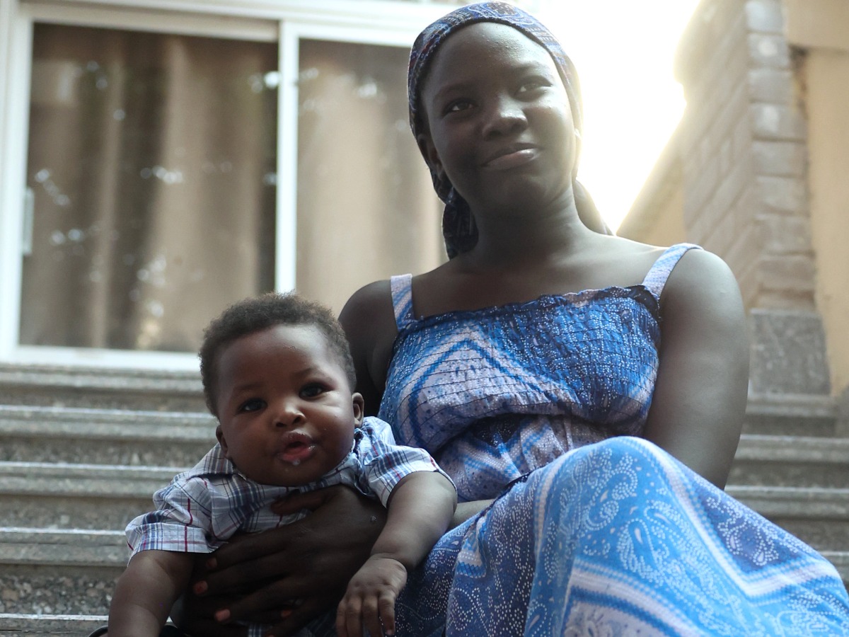 A woman holding a baby smiles to the camera