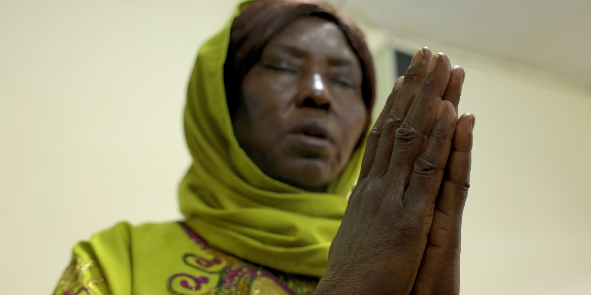 A woman wearing yellow headscarf, eyes closed, praying