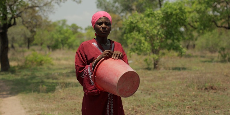 A woman in traditional African dress holding a bucket