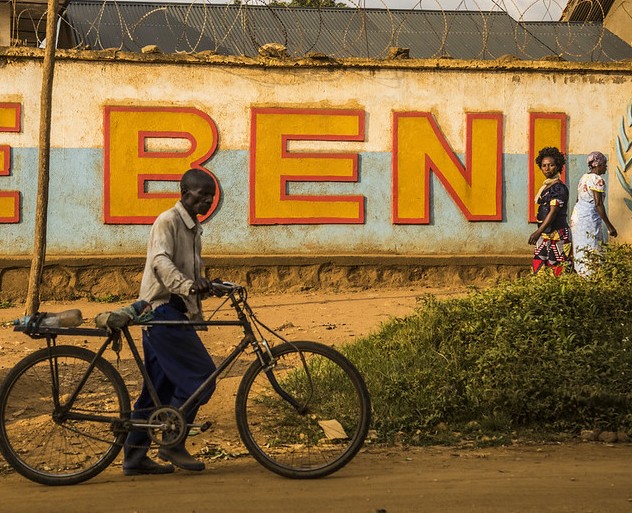 A man wheeling a bike in front of a wall with the word BENI painted on