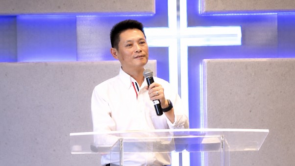 Dark haired man preaching in front of cross