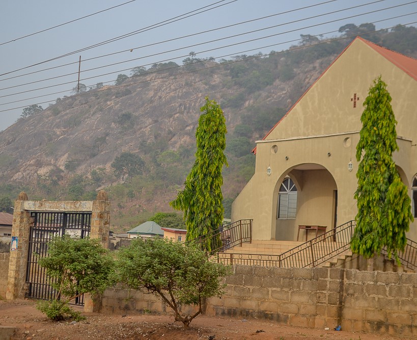A beige building with a red roof in front of a rocky landscape