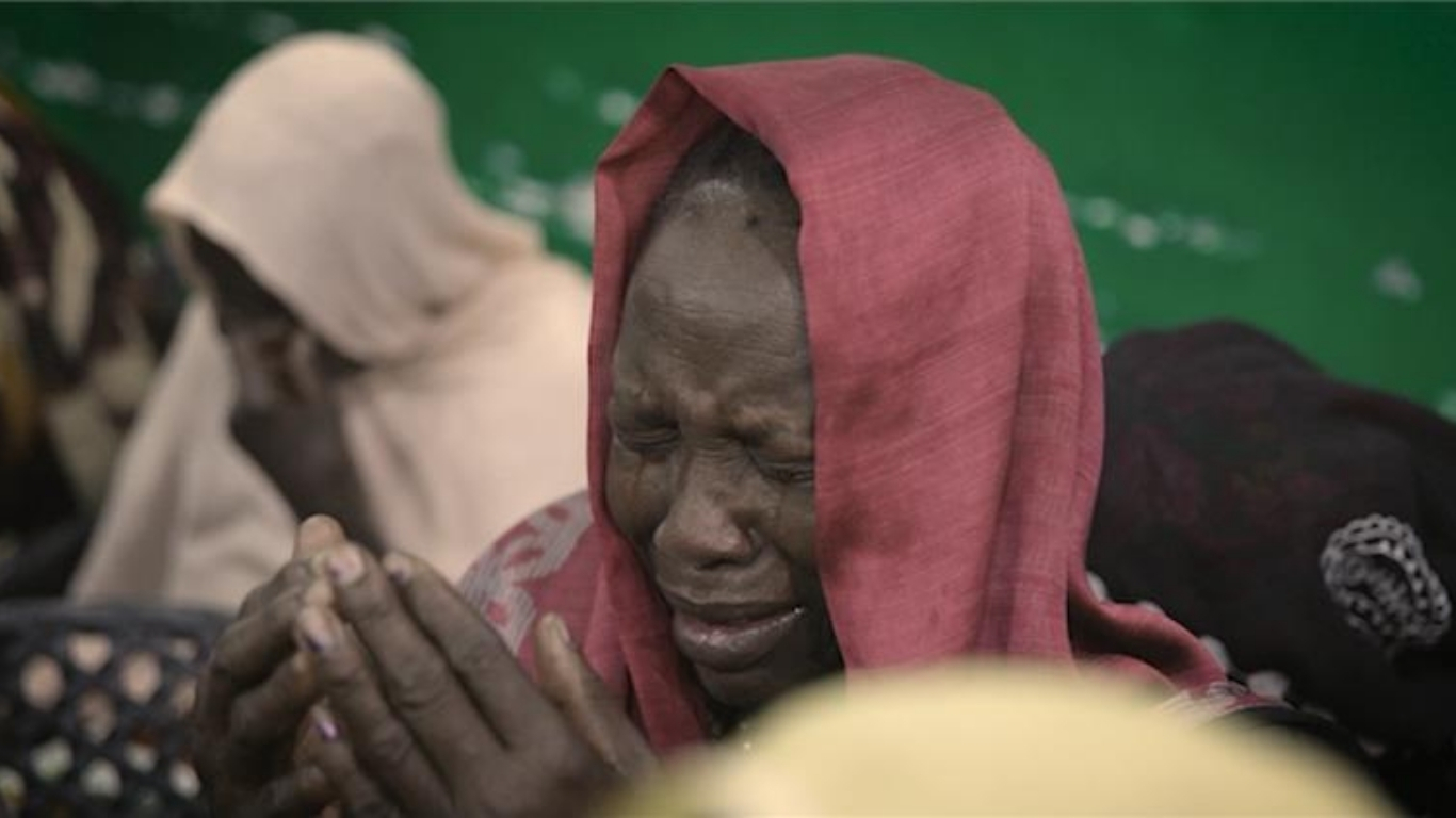 Sudanese Christian woman wearing a red shawl is visibly crying, conveying a sense of sadness and distress.