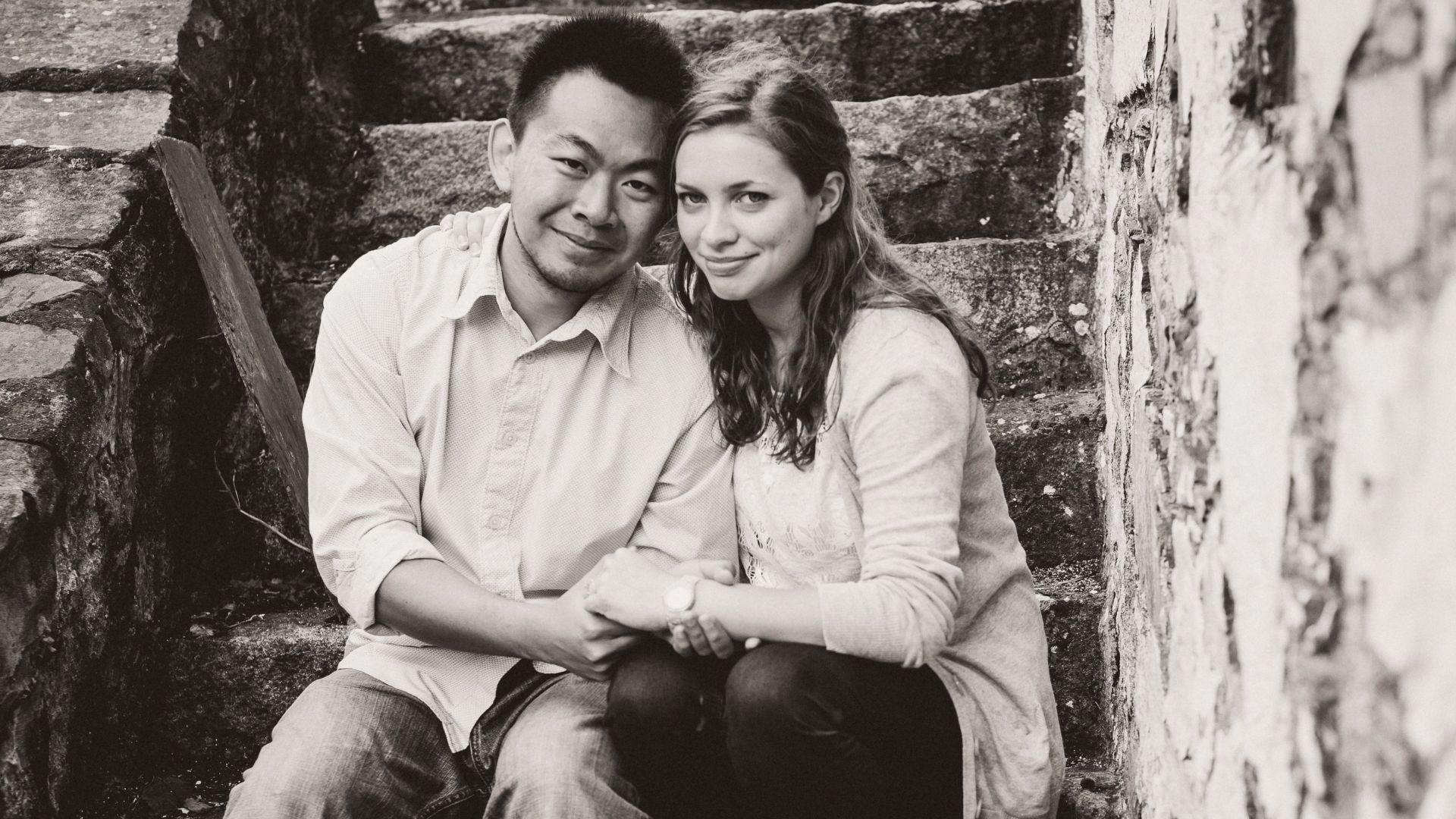 Timothy and Sarah are seated on stone steps, with a textured stone wall behind them, capturing a moment of companionship.