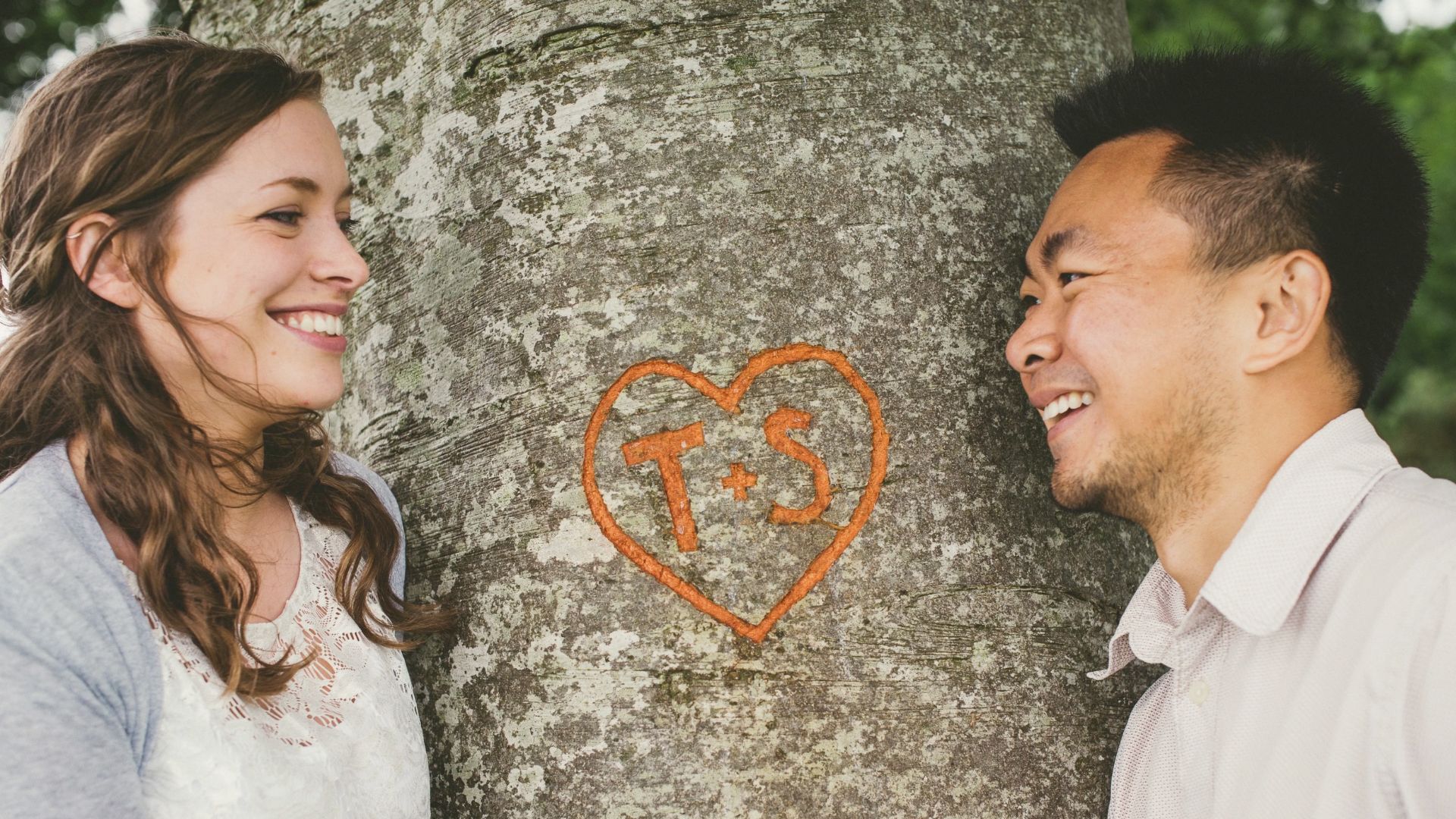 Timothy and Sarah look at each other, with a tree featuring their initials carved in a heart.