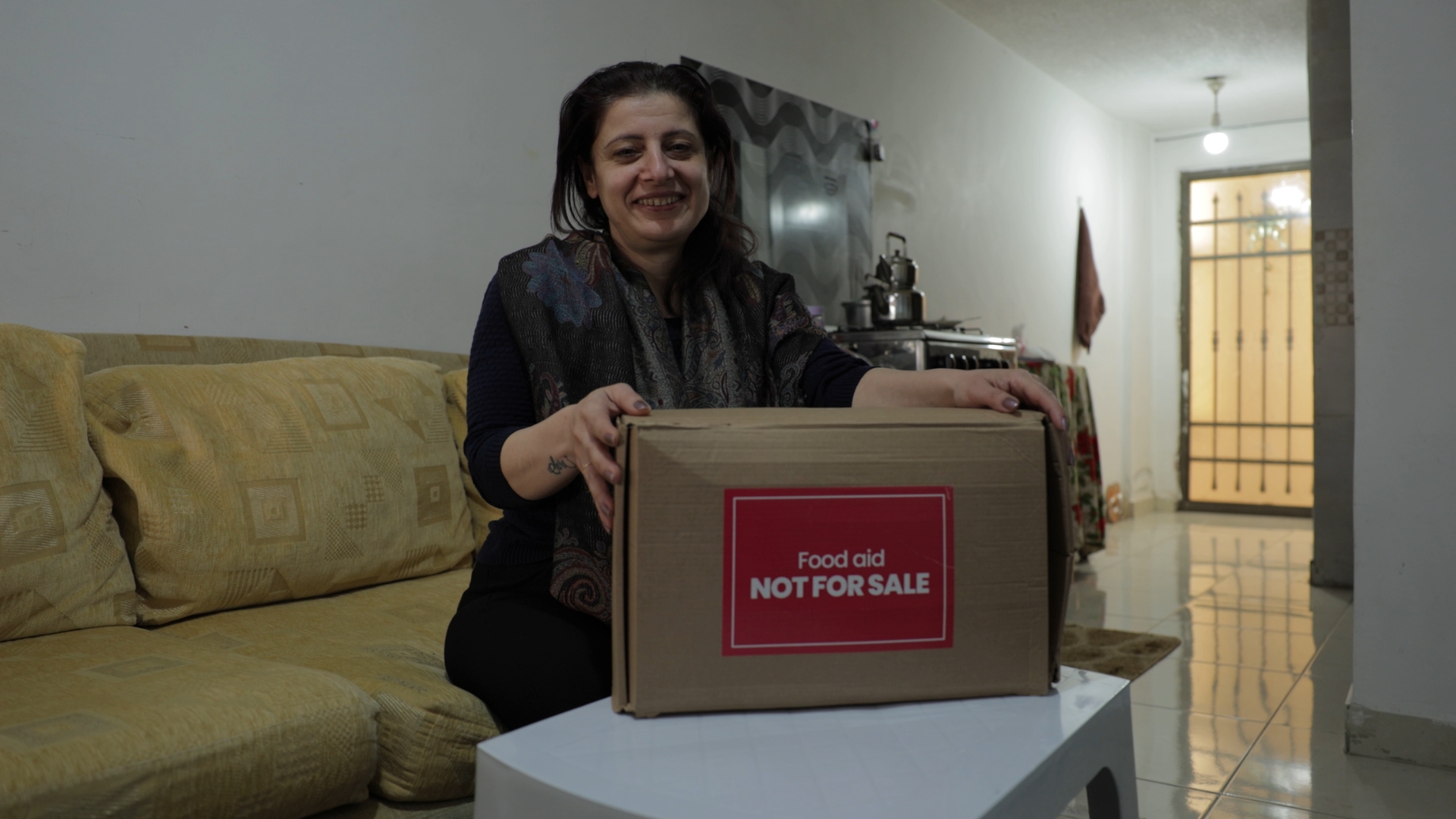 An Iraqi Christian named Rania holds a food aid box marked with a prominent red sign, symbolising support and assistance.