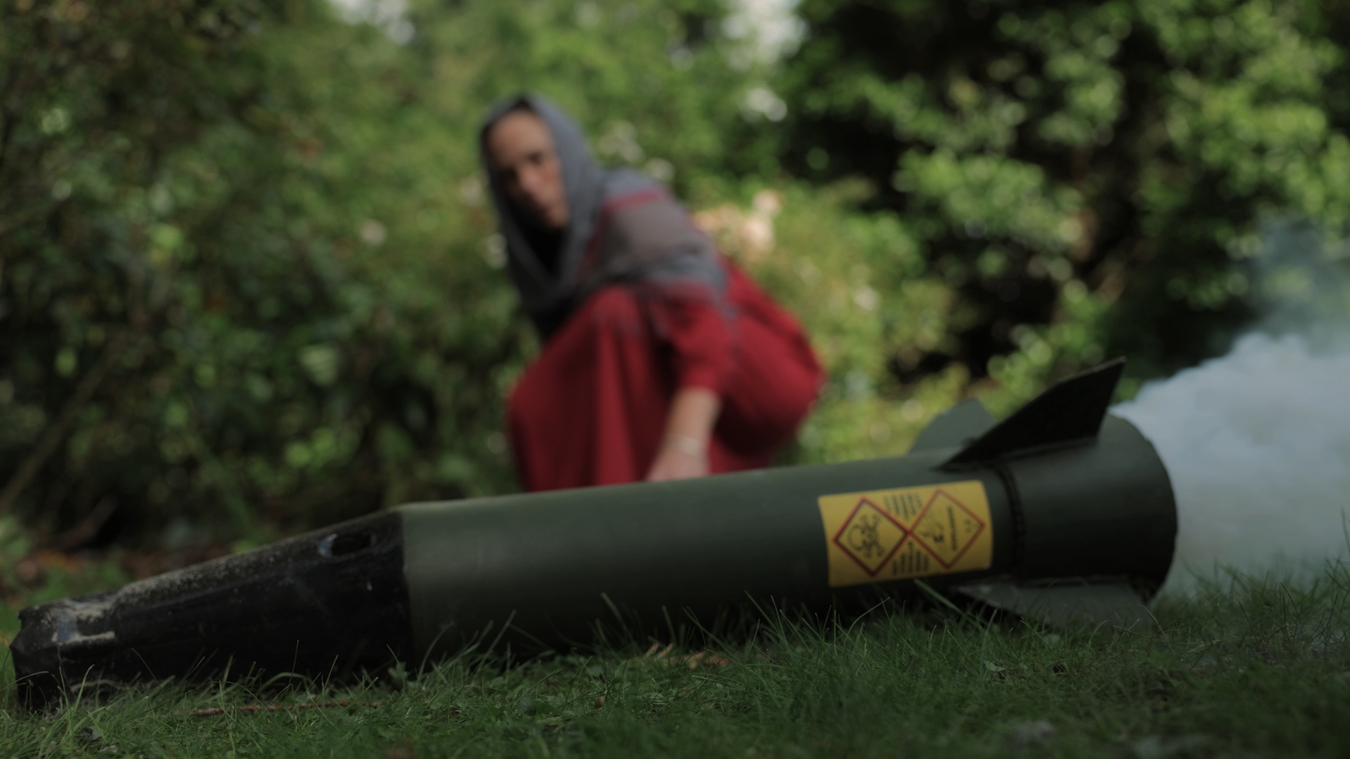 A startled woman kneels beside a large green rocket, looking as if she is about to run away.
