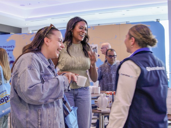 Two young women speaking with a third woman wearing a "Barnabas Aid" top
