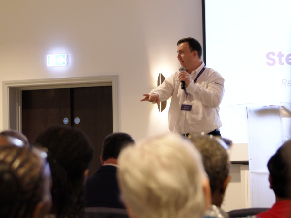 A man in white shirt speaking to a group of people
