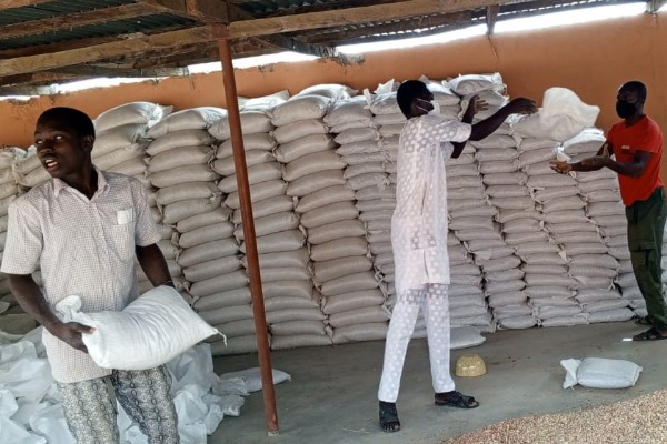 Three men moving bags of food from a pile in a storeroom