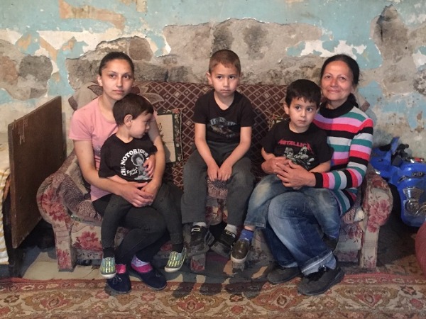 Three young boys with their mother and grandmother on an old sofa in a dilapidated home
