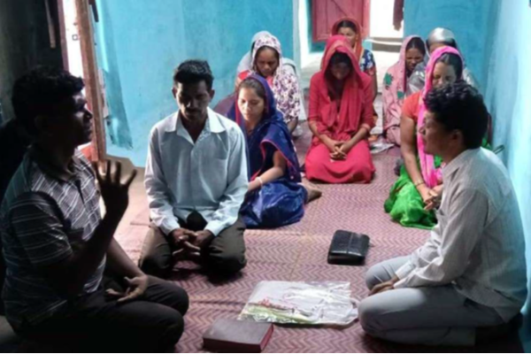 A group of men and women, inside a house, kneeling in prayer