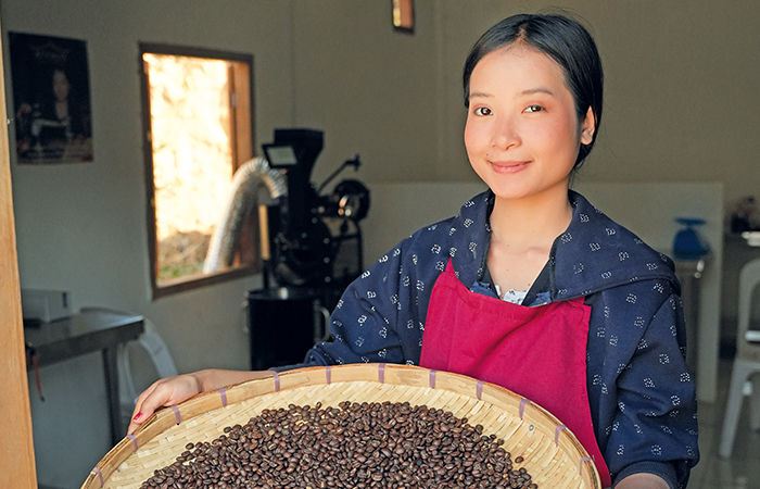 A woman wearing a red apron holding a large bowl of coffee beans
