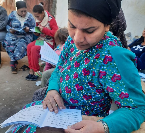A woman in a turquoise dress in a class room reading a work book