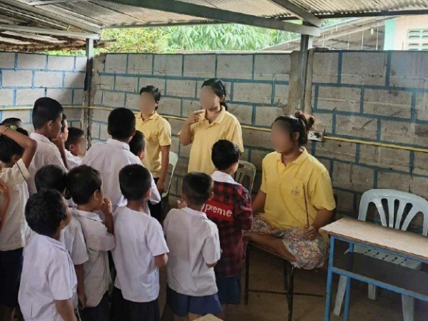 A teacher engages with a group of children in yellow shirts, highlighting a caring educational setting rooted in faith.