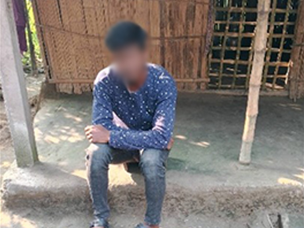 A young man sat on a step in front of a very basic wooden hut