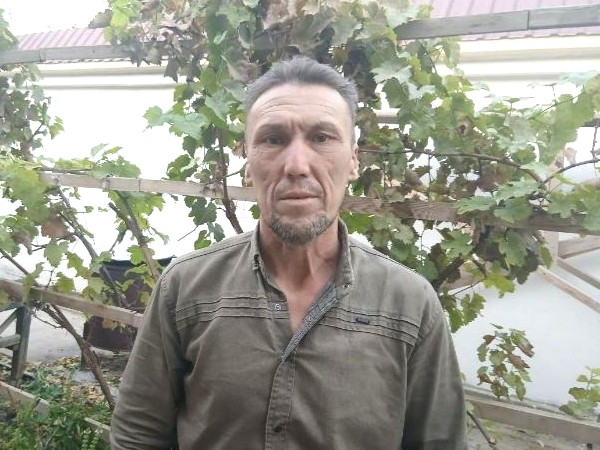 A middle aged man in a rural setting wearing a khaki shirt