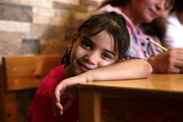 A young girl with dark hair looks directly at the camera