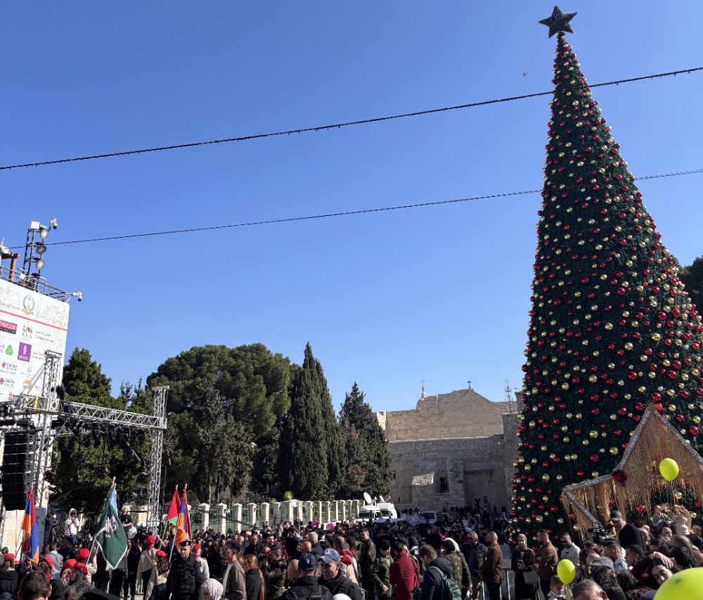 A crowd of people around a Christmas tree with a star on top