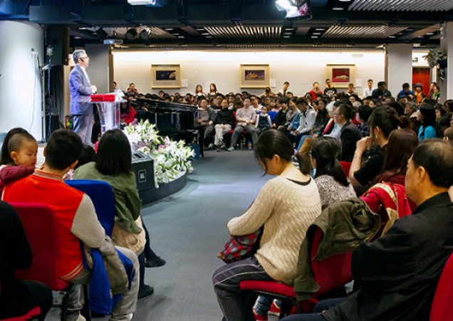 A man in a grey suit at a lectern addressing a room full of people