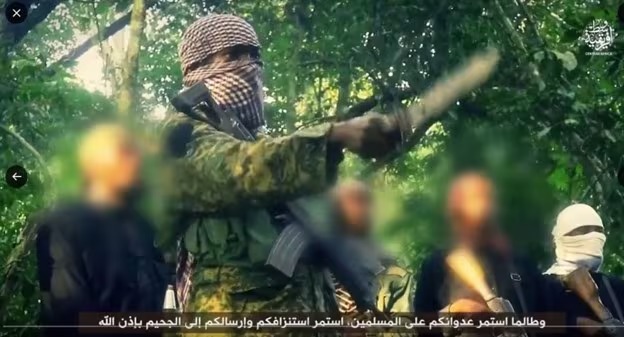 A man with face hidden in military camouflage holding a machine gun and pointing a knife