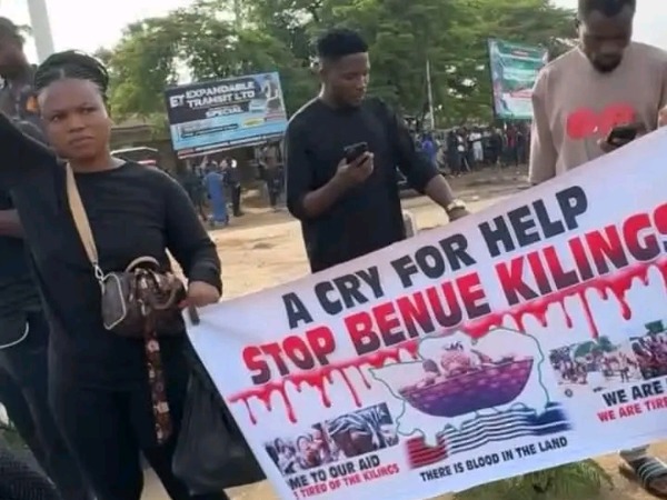 Three people holding a banner with the words: A cry for help. Stop Benue killings.