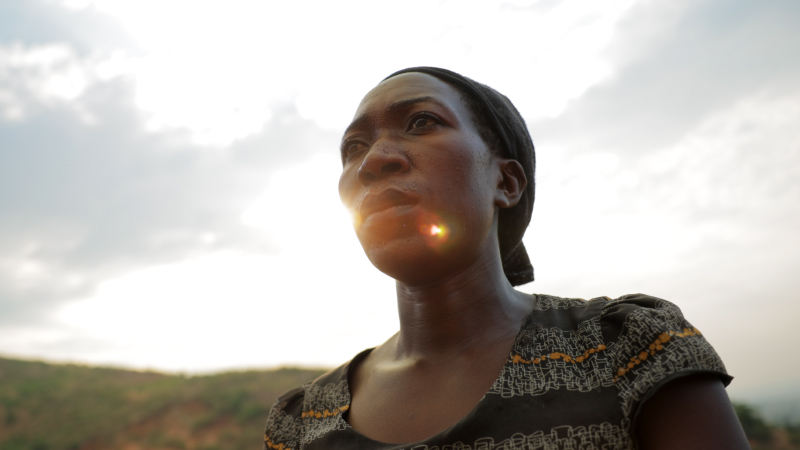 Angela, A Christian woman stands confidently against a bright, sunlit sky, surveying the unfarmed land that needs so much work.